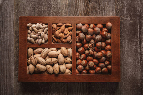 вид сверху на ассортимент различных орехов в коробке на деревянном фоне
