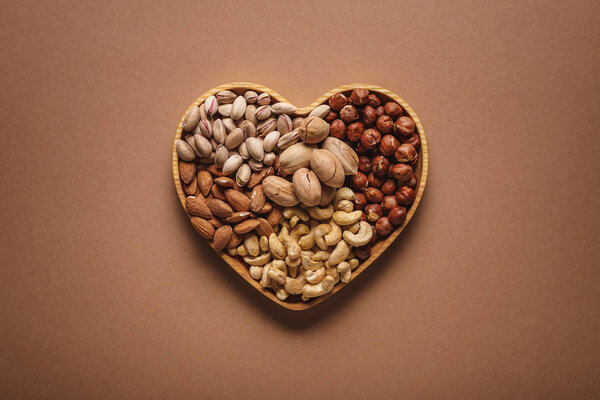 top view of assortment of various nuts in heart shaped box on brown backdrop