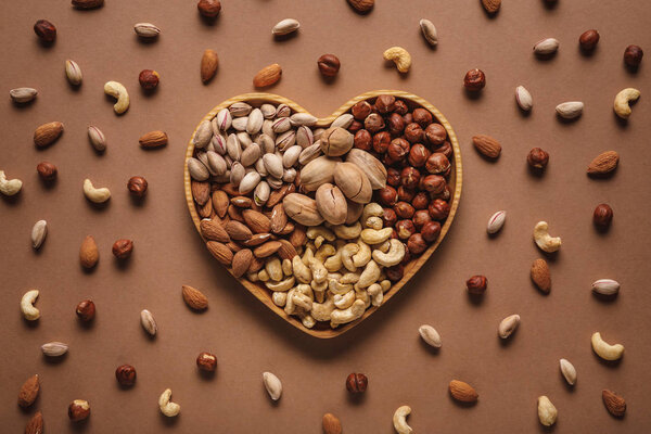 flat lay with heart shaped box with different nuts assortment on brown tabletop