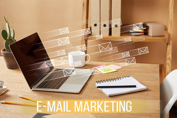 laptop with email icons and "email marketing" lettering on wooden table at home