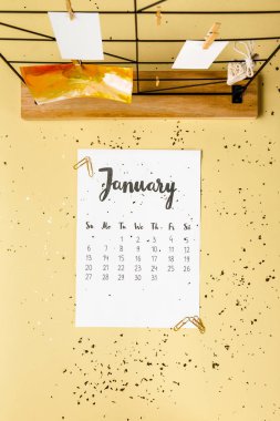 top view of january calendar with golden confetti and cards with clothespins on beige clipart