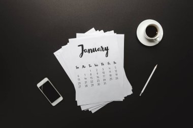 top view of january calendar, smartphone, pencil and cup of coffee on black clipart