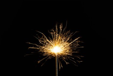 close-up view of burning and glowing new year sparkler on black background clipart