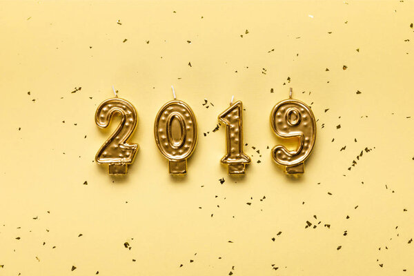 золотые свечи 2019 года и праздничные конфетти на бежевом фоне
