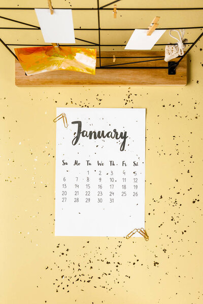 top view of january calendar with golden confetti and cards with clothespins on beige