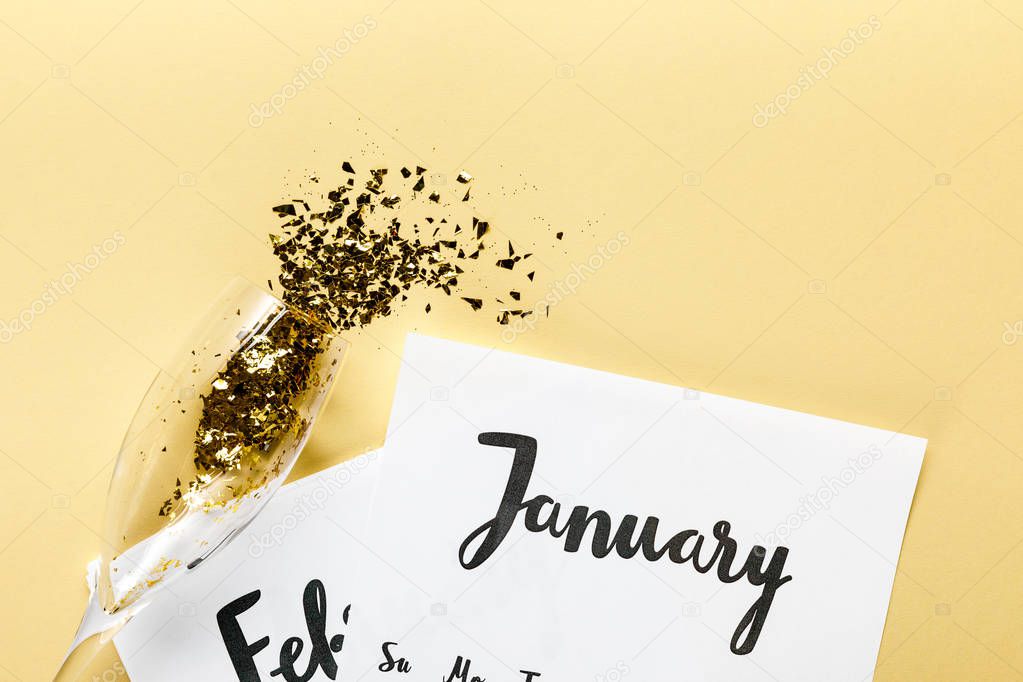 champagne glass with golden confetti, papers with january and february calendar on beige background  
