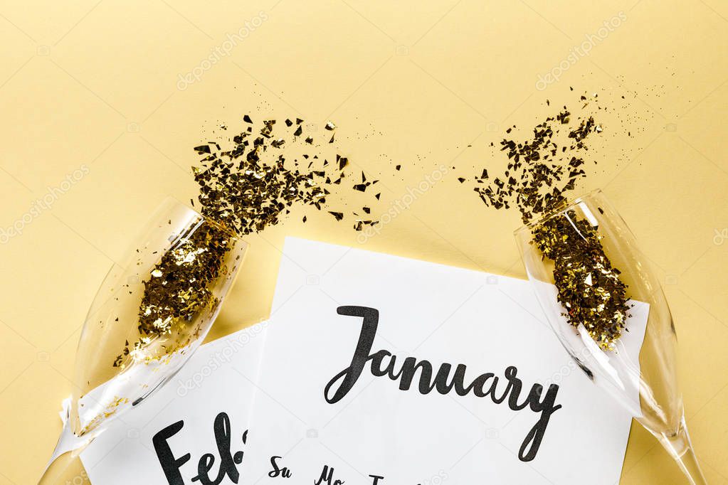 champagne glasses with golden confetti, papers with january and february calendar on beige background  