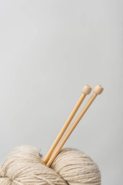 close up view of beige knitting clews with knitting needles on grey backdrop clipart