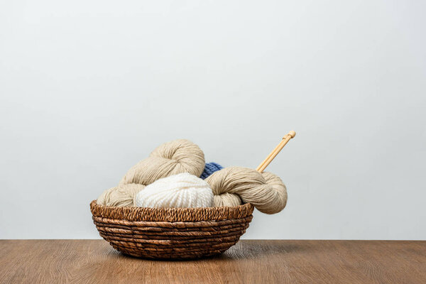 close up view of yarn with knitting needles in wicker basket on wooden tabletop on grey background