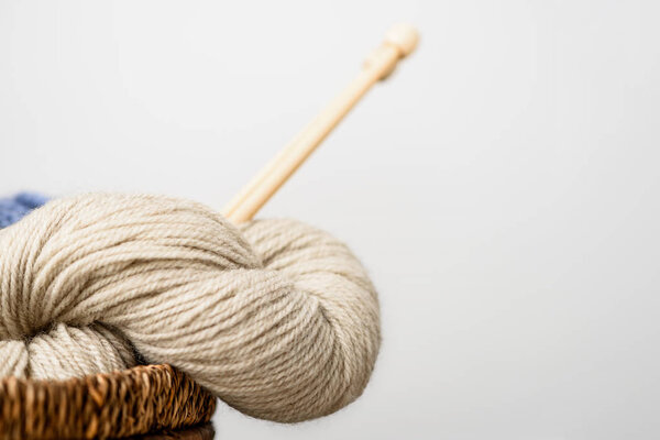 close up view of beige yarn with knitting needles on grey background