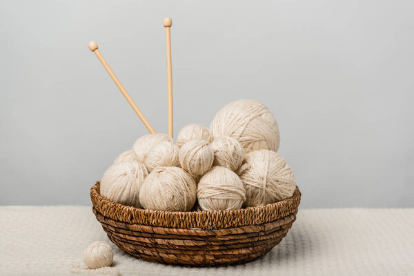 close up view of yarn clews and knitting needles in wicker basket on grey background