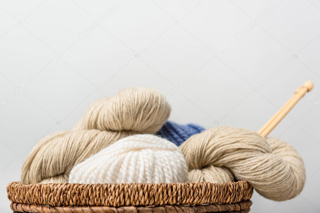close up view of knitting with knitting needles in wicker basket on grey backdrop