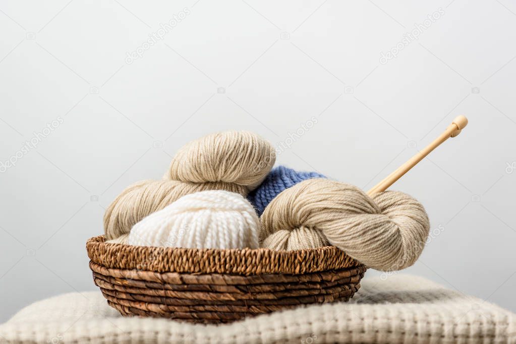 close up view of yarn with knitting needles in wicker basket on grey backdrop