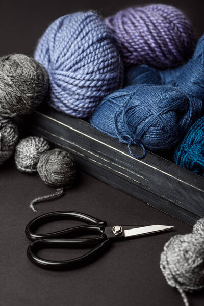 закрывающийся вид серых, фиолетовых и синих вязальных клюшек в деревянной коробке на сером столе с ножницами
