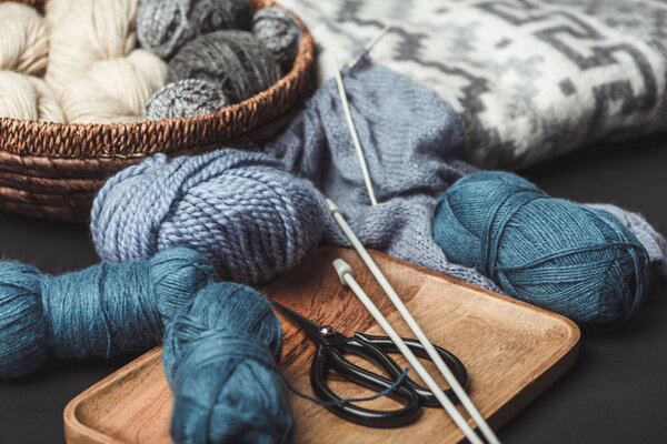 close up view of knitting, scissors and knitting needles on dark tabletop with blanket