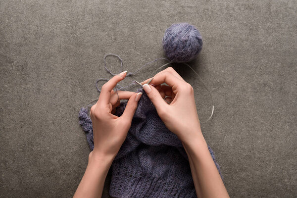 partial view of woman knitting yarn on grey backdrop