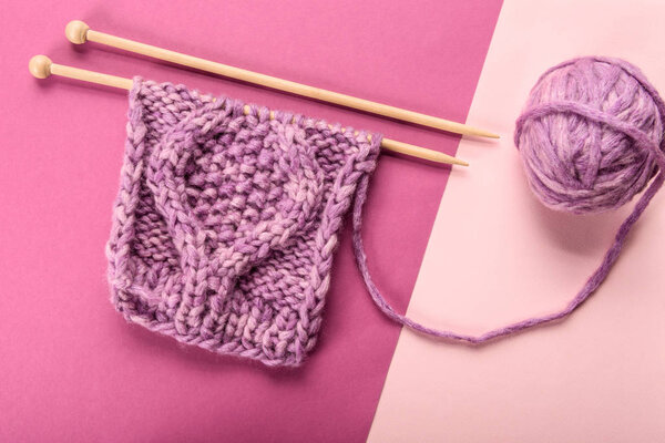 flat lay with purple yarn ball and knitting needles on pink and purple backdrop