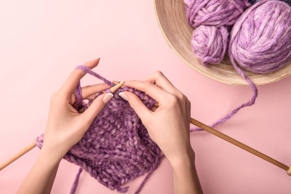 partial view of woman knitting yarn on pink background