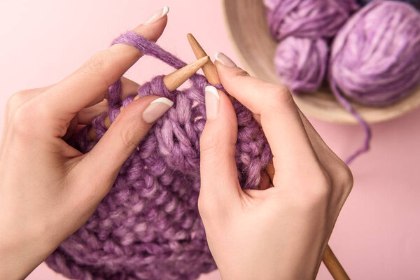 partial view of woman knitting yarn on pink background