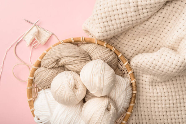 top view of yarn in wicker basket on pink background with knitted blanket 