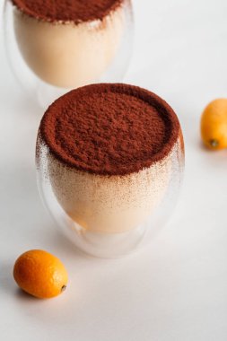 tiramisu desserts with cocoa powder in glasses on grey table with kumquats clipart