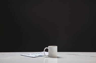 white cup and travel newspaper on black background clipart