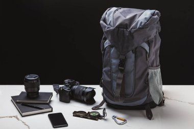 backpack, smartphone, compass, notebooks and photo camera with lens on black clipart