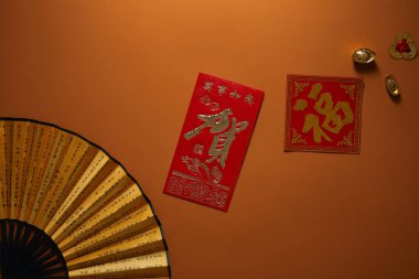 top view of fan with hieroglyphs and golden decorations on brown background, chinese new year composition clipart