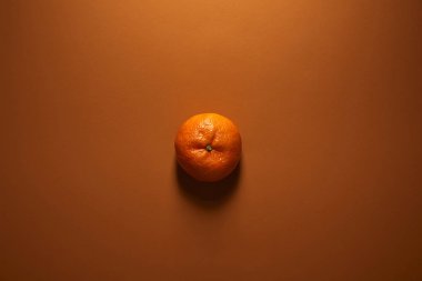 top view of whole single ripe tangerine on brown background clipart
