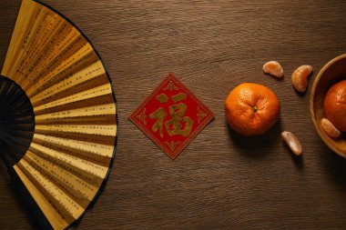 top view of fan, fresh ripe tangerines and decorative golden hieroglyph on wooden table clipart