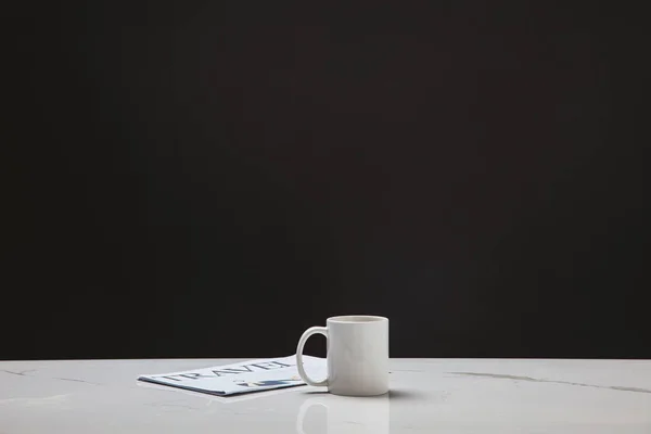 white cup and travel newspaper on black background