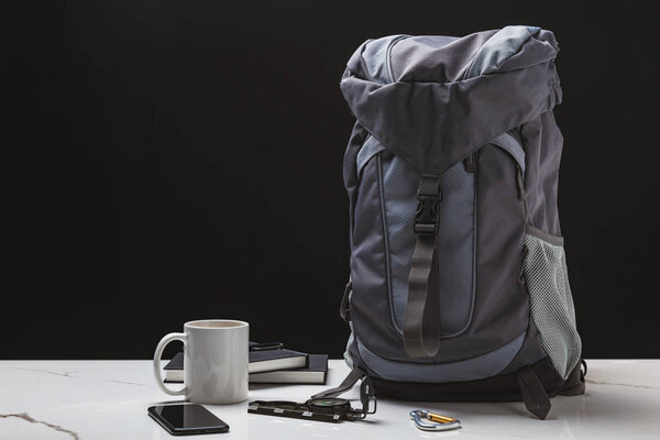 backpack, smartphone, cup, notebooks and compass on black, travel concept 
