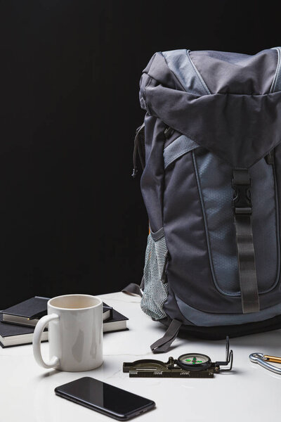 backpack, smartphone, cup and compass on black, travel concept 