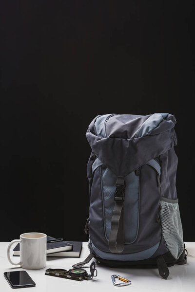 backpack, cup, notebooks, smartphone and trekking equipment on black