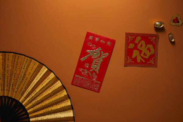 top view of fan with hieroglyphs and golden decorations on brown background, chinese new year composition