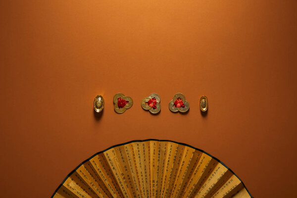 вид на традиционные золотые китайские украшения и веер с иероглифами на коричневом фоне
  