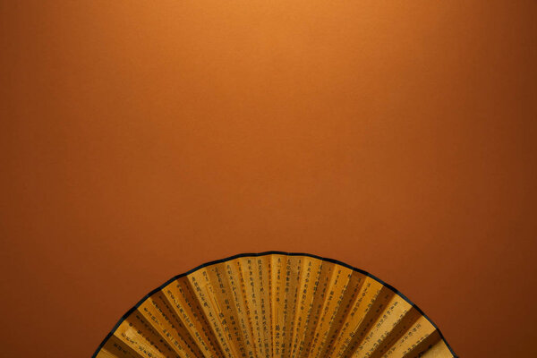 вид на традиционный золотой китайский веер с иероглифами на коричневом фоне
