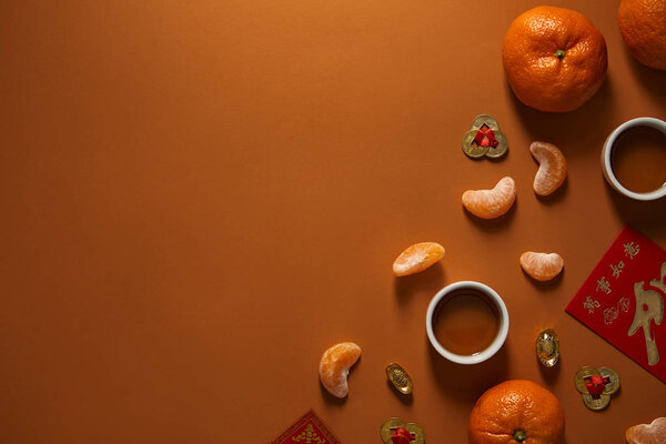 top view of fresh ripe tangerines, cups of tea and traditional chinese decorations on brown background