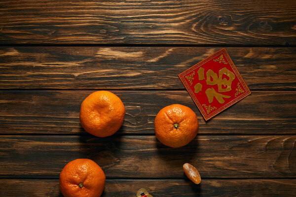 top view of fresh ripe tangerines and golden hieroglyph on red on wooden table