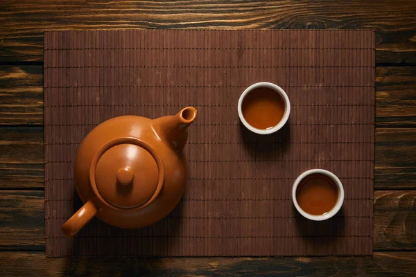 Draufsicht Auf Braune Keramik Teekanne Und Tassen Tee Auf Bambusmatte — Stockfoto