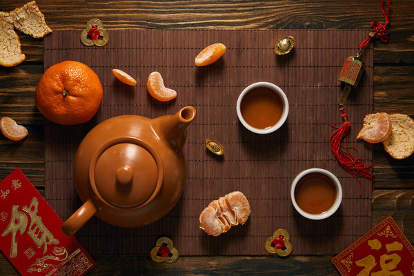top view of tea set, tangerines and traditional chinese decorations on bamboo mat