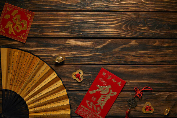 top view of chinese new year composition with fan, hieroglyphs and decorative golden coins on wooden surface