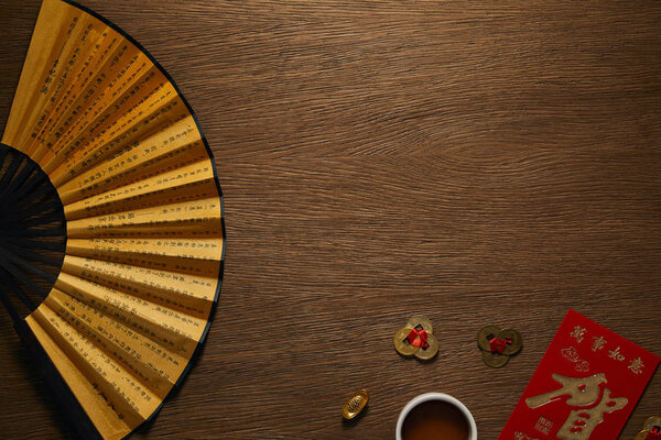 top view of fan with hieroglyphs, golden coins and cup of tea on wooden table