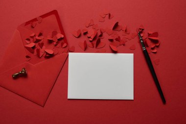 top view of empty white letter with envelope, paper cut hearts and pen on red background clipart