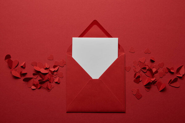 top view of blank white letter in envelope with paper cut hearts on red background