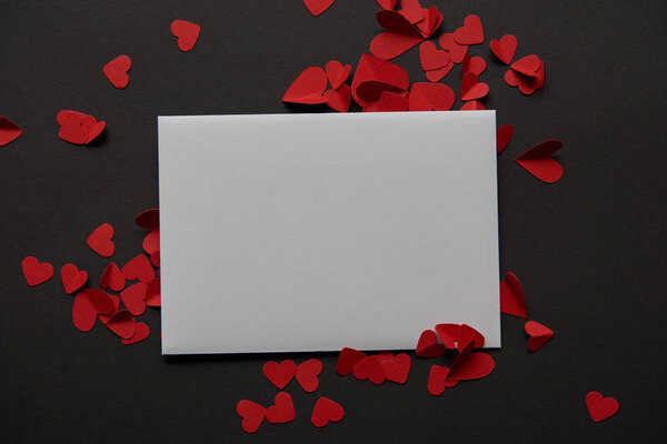 top view of white empty greeting card and red paper cut hearts on black background