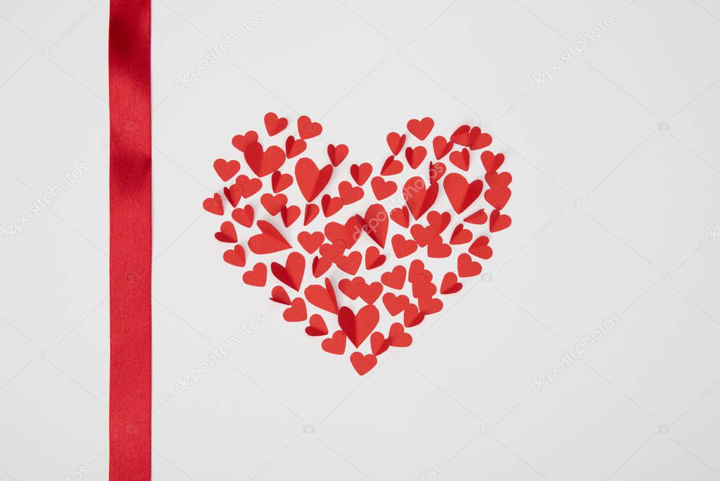 heart shaped arrangement of small red paper cut hearts with satin ribbon on white background