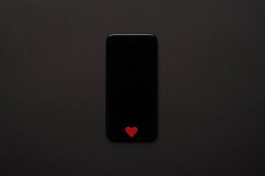 üstten görünüm Smartphone ile boş perde ve küçük kırmızı kalp koyu arka plan üzerinde oturum