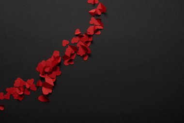 üstten görünüm kırmızı küçük kağıt kalpler siyah arka plan üzerine kesilmiş. 