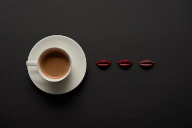 top view of cup of coffee near chocolate lips on black background clipart